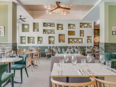 Ristorante elegante con tavoli moderni e sedie verdi, decorato con scaffali a parete e opere d'arte.