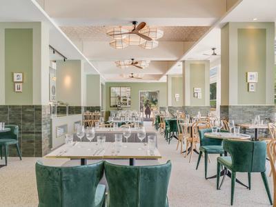 Elegante ristorante dell'hotel con sedie verdi imbottite e tavoli bianchi sotto luci moderne.