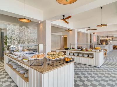 Buffet moderno con pasticceria assortita e aree salotto aperte in un ristorante luminoso.