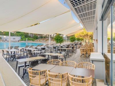 Grande terrazza con tavoli e sedie sotto tende da sole accanto a una piscina al crepuscolo.