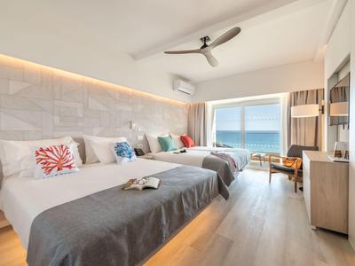 Camera d'albergo moderna con due letti matrimoniali, vista mare e pavimento in legno chiaro.