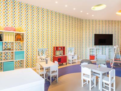 Sala giochi per bambini luminosa e colorata con tavoli, sedie e scaffali in un hotel.