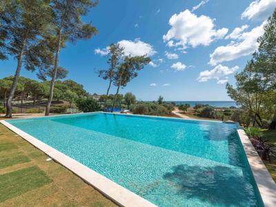 Piscina esterna moderna vicino a pini con vista mare e cielo azzurro.