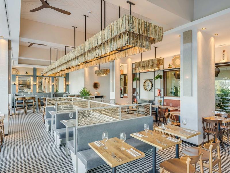 Caffetteria moderna con mobili in legno e metallo, grandi finestre e un lungo lampadario.