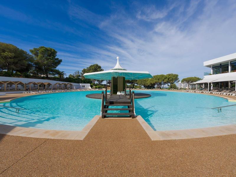 Grande piscina all'aperto con ombrelloni e lettini sotto un cielo azzurro in un hotel.