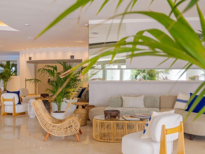 Area lounge dell'hotel luminosa e moderna con piante, mobili in vimini e posti a sedere.