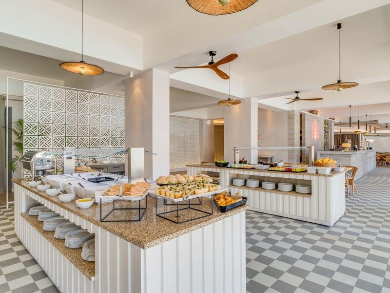 Buffet moderno con pasticceria assortita e aree salotto aperte in un ristorante luminoso.