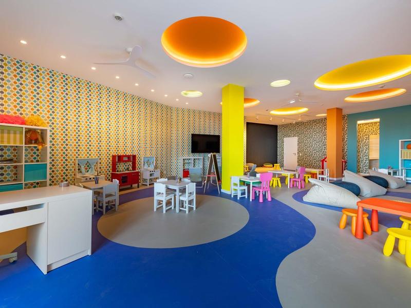 Area giochi colorata per bambini con piccoli tavoli, sedie e sgabelli in un hotel.
