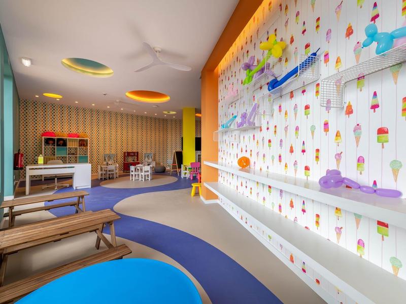 Colorata sala giochi con posti a sedere, parete da arrampicata e moquette in un hotel.