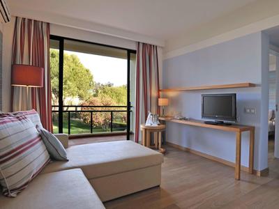 Lichte woonkamer met bank, groot raam, bureau met tv en uitzicht op groen.