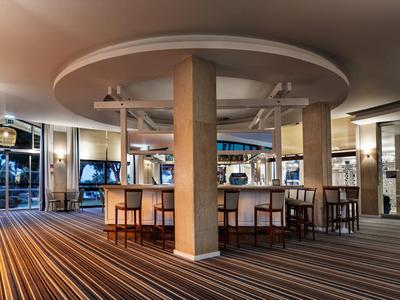 Lichte hotel lounge met een centrale bar, zuilen en gestreepte tapijtvloer.