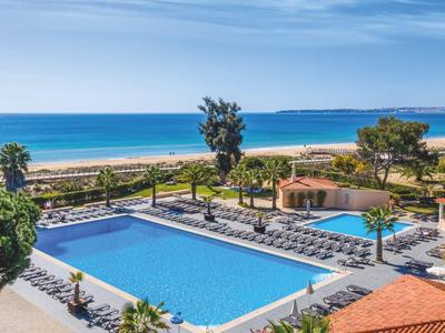 Uitzicht op een hotelzwembad met zeezicht en blauwe lucht bij het strand.