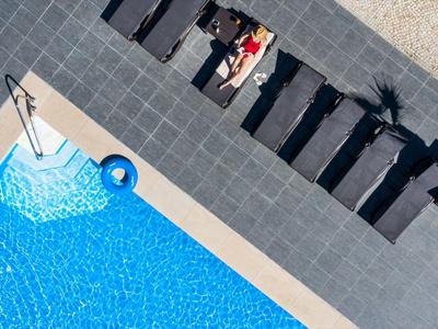 Blick von oben auf einen blauen Hotelpool mit Liegestühlen und einer Person im Schatten.