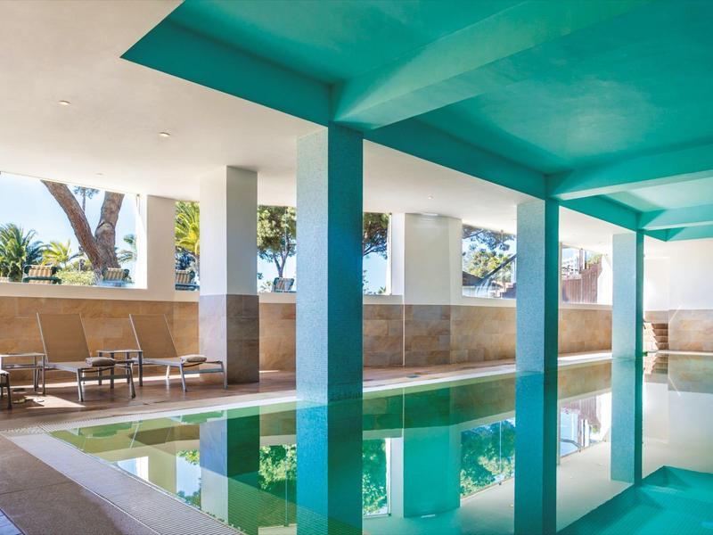 Overdekt zwembad met turquoise plafondbalken en zithoek in hotel.