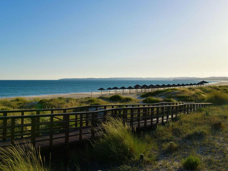 Zonsopgang boven een lange houten loopbrug op het strand met uitzicht op zee en duinen.