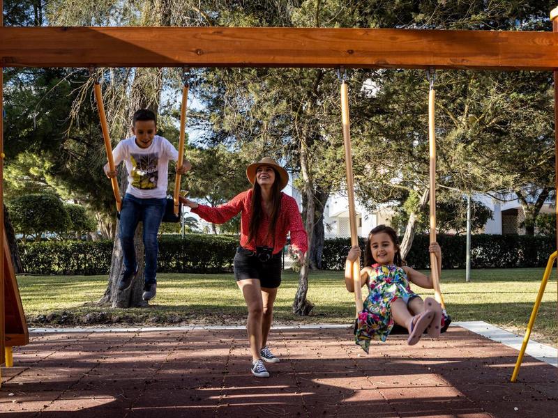 Drie kinderen spelen op een houten schommelset in een zonnig park.