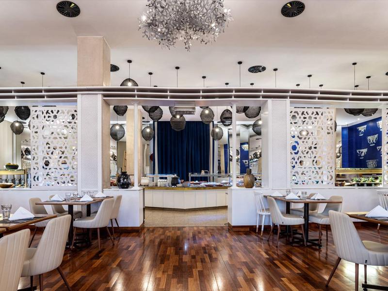 Elegant restaurant met houten vloeren, witte stoelen, gedekte tafels en moderne verlichting.