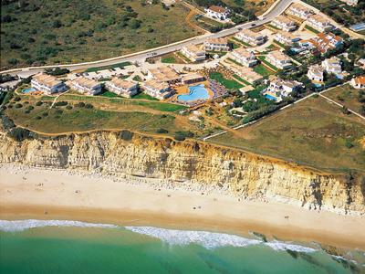 Luftaufnahme von Häusern und einem Pool auf einer Klippe über einem Strand mit grünem Meer.