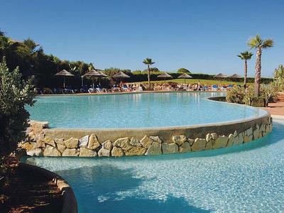 Runder Pool mit Steinmauer und Palmen bei sonnigem Himmel im Hotelgarten.