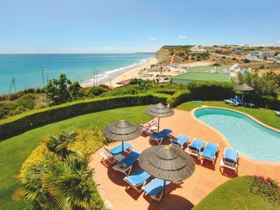 Hotelpool mit Liegestühlen und Sonnenschirmen, Meer und Strand im Hintergrund.