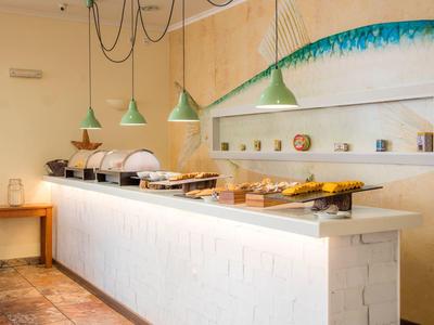 Buffetbereich mit geschlossenen Essensbehältern und Tassen in einem hellen Raum mit grünen Hängelampen.