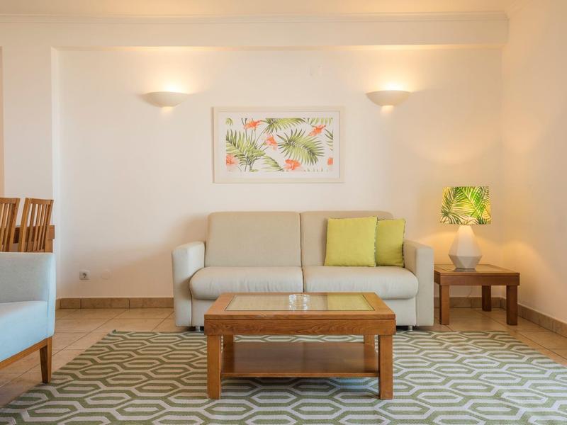 Helles Wohnzimmer mit grauem Sofa, Holztisch und buntem Wandbild, gemütliche Atmosphäre.