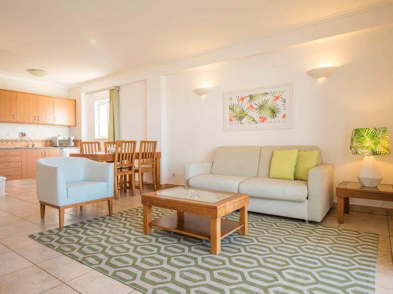 Helles Wohnzimmer mit Sofa, Sessel, Teppich und Essbereich in einem modernen Apartment.