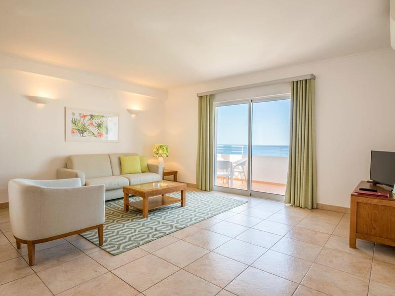 Helles Wohnzimmer mit großen Fenstern, beigem Sofa, Holzmöbeln und Meerblick.