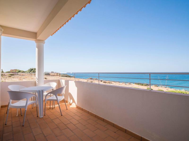 Balkon mit weißen Stühlen und Tisch, Blick auf Meer unter klarem blauem Himmel.