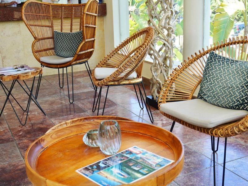 Gemütliche Sitzecke mit Rattanstühlen, hölzernem Tisch, bodentiefen Fenstern und Ziegelboden.