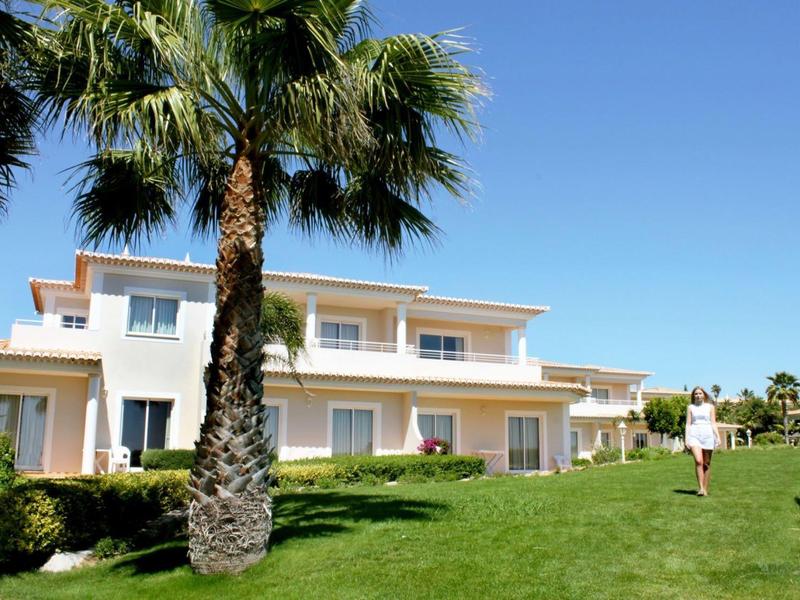 Moderne, weiße Ferienhäuser mit großem grünen Rasen und einer Palme unter blauem Himmel.