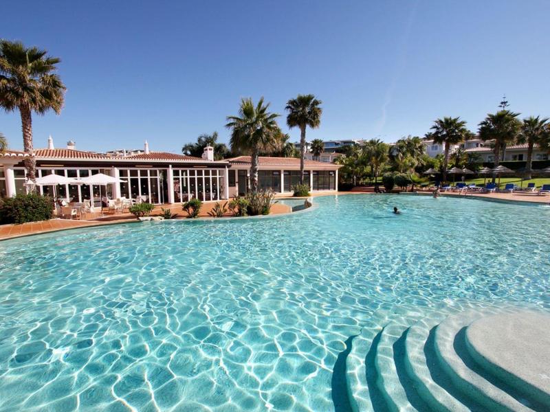 Großer Hotelpool mit klar blauem Wasser, Stufen und Palmen bei sonnigem Himmel.
