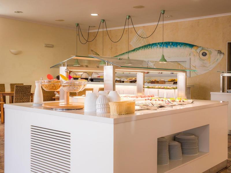 Hotelbuffet mit Müsli und warmen Speisen in hellen Speisesaal mit Fisch-Wanddekoration.