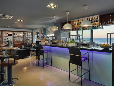 Moderner Barraum mit Theke, hohen Stühlen, Regalen voller Flaschen und Meerblick durch Fenster.