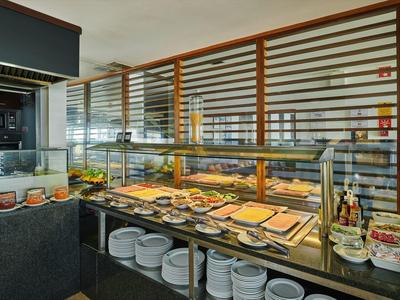 Buffet mit gedeckten Tellern, Besteck, frischem Obst und warmen Speisen hinter Glasvitrine.