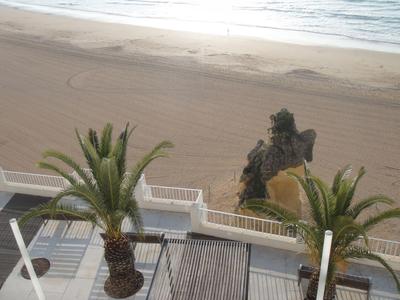 Strand mit Palmen, Holzsteg und Felsen am Sandstrand unter bewölktem Himmel.