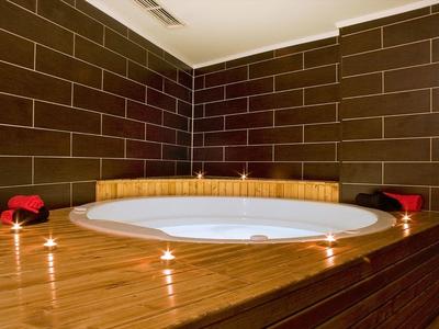 Rundes Whirlpool-Becken in Holzumrahmung, umgeben von braunen Fliesen und brennenden Teelichtern.