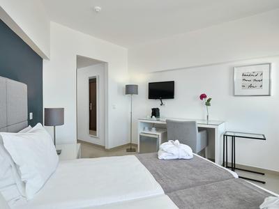 Modernes Hotelzimmer mit weißer Einrichtung, grauen Akzenten, Bett, Schreibtisch und Fernseher.
