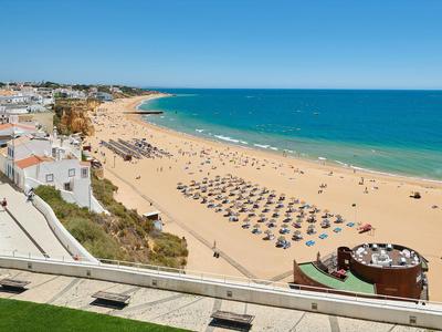 Breiter Sandstrand mit Sonnenschirmen, blauem Meer und Häusern im Hintergrund unter klarem Himmel.