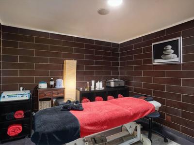 Ruhiger Massageraum mit roter Liege, braunen Wandfliesen, sanfter Beleuchtung und Wellnessdekor.