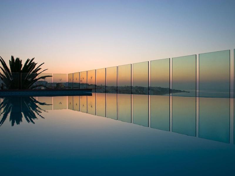 Ein ruhiger Pool spiegelt Glasgeländer und Palmen bei Sonnenuntergang wider.