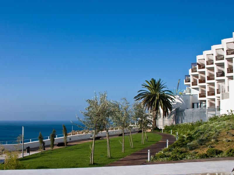 Küstenblick mit Palmen, Rasen und weißem Gebäude unter blauem Himmel.