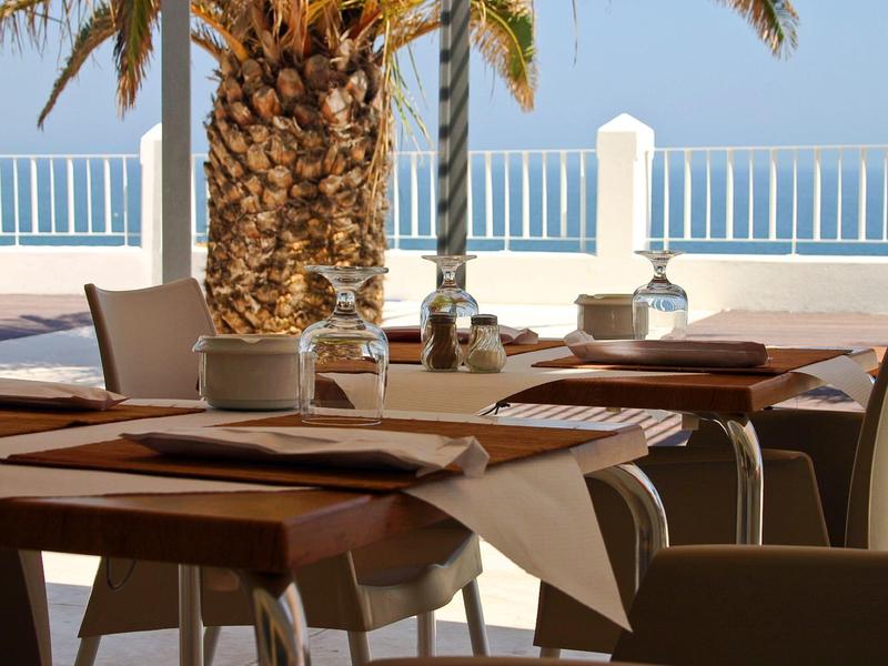 Buffet mit gedeckten Tellern, Besteck, frischem Obst und warmen Speisen hinter Glasvitrine.