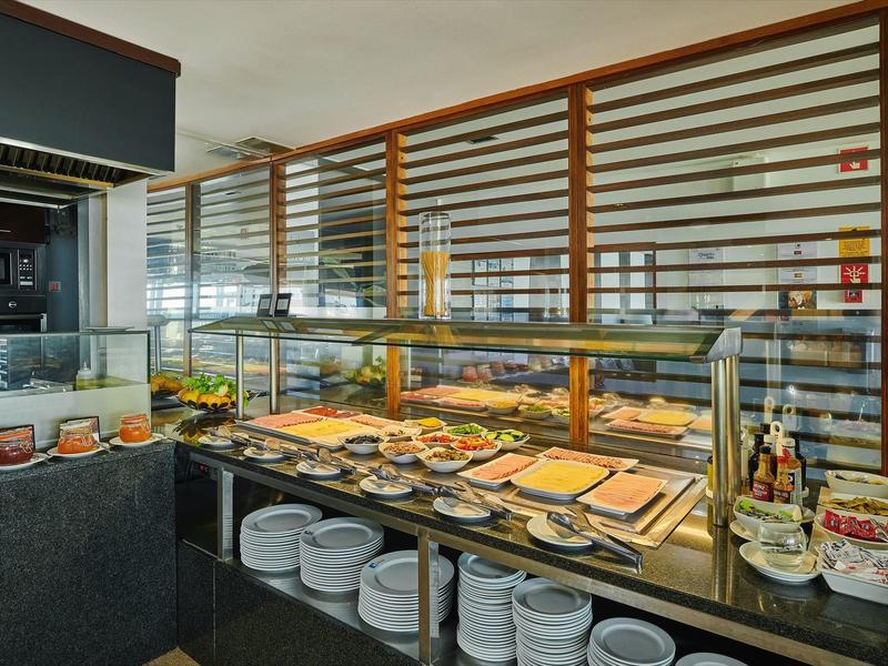 Buffet mit gedeckten Tellern, Besteck, frischem Obst und warmen Speisen hinter Glasvitrine.
