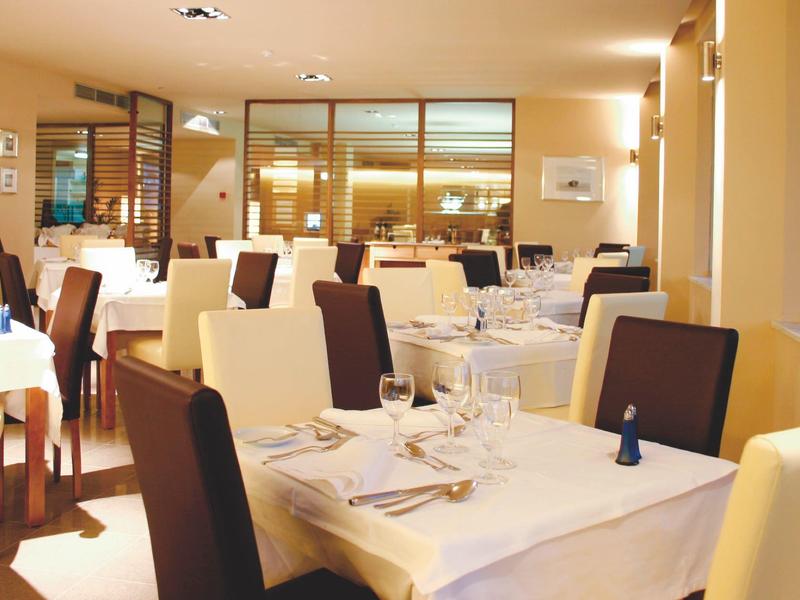 Helles, modernes Restaurant mit weißen Tischdecken, Holzstühlen und warmem Beleuchtungskonzept.