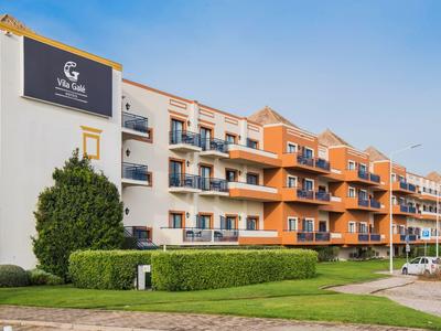 Mehrstöckiges Wohngebäude mit Balkonen, weißen und orangefarbenen Fassaden, umgeben von Grünflächen.