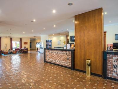 Großer Hotel-Empfangsbereich mit Rezeptionstresen, Sitzgruppen und warmen Holzakzenten.