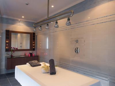 Moderner Wellnessraum mit Massagebank, Grauwänden, Spiegel, Handtüchern und indirektem Licht.