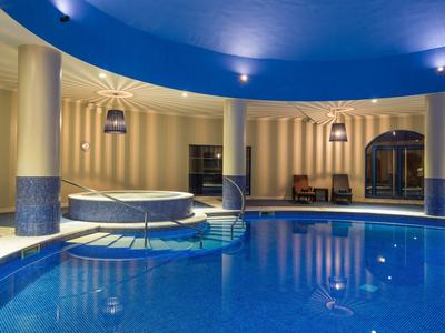 Runder, blauer Hallenpool mit integriertem Whirlpool, Säulen und abgerundetem blauen Deckendach.