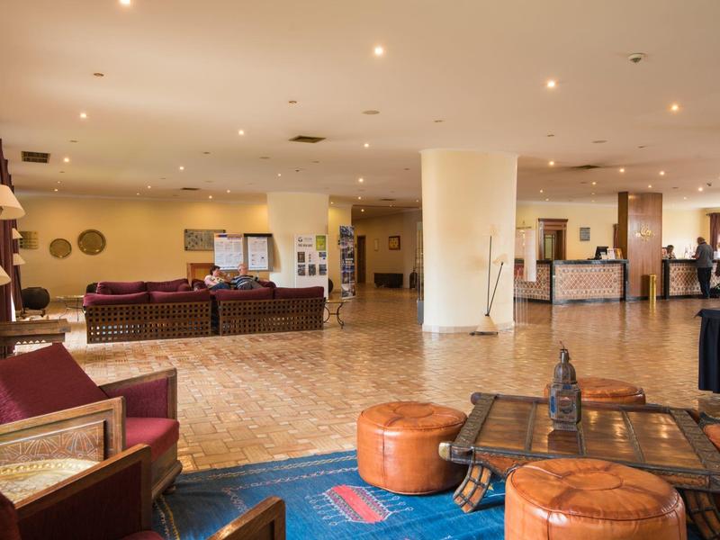 Großer, heller Hotel-Lobbybereich mit Sesseln, Sofas, Tischen und Teppichen in warmen Farben.